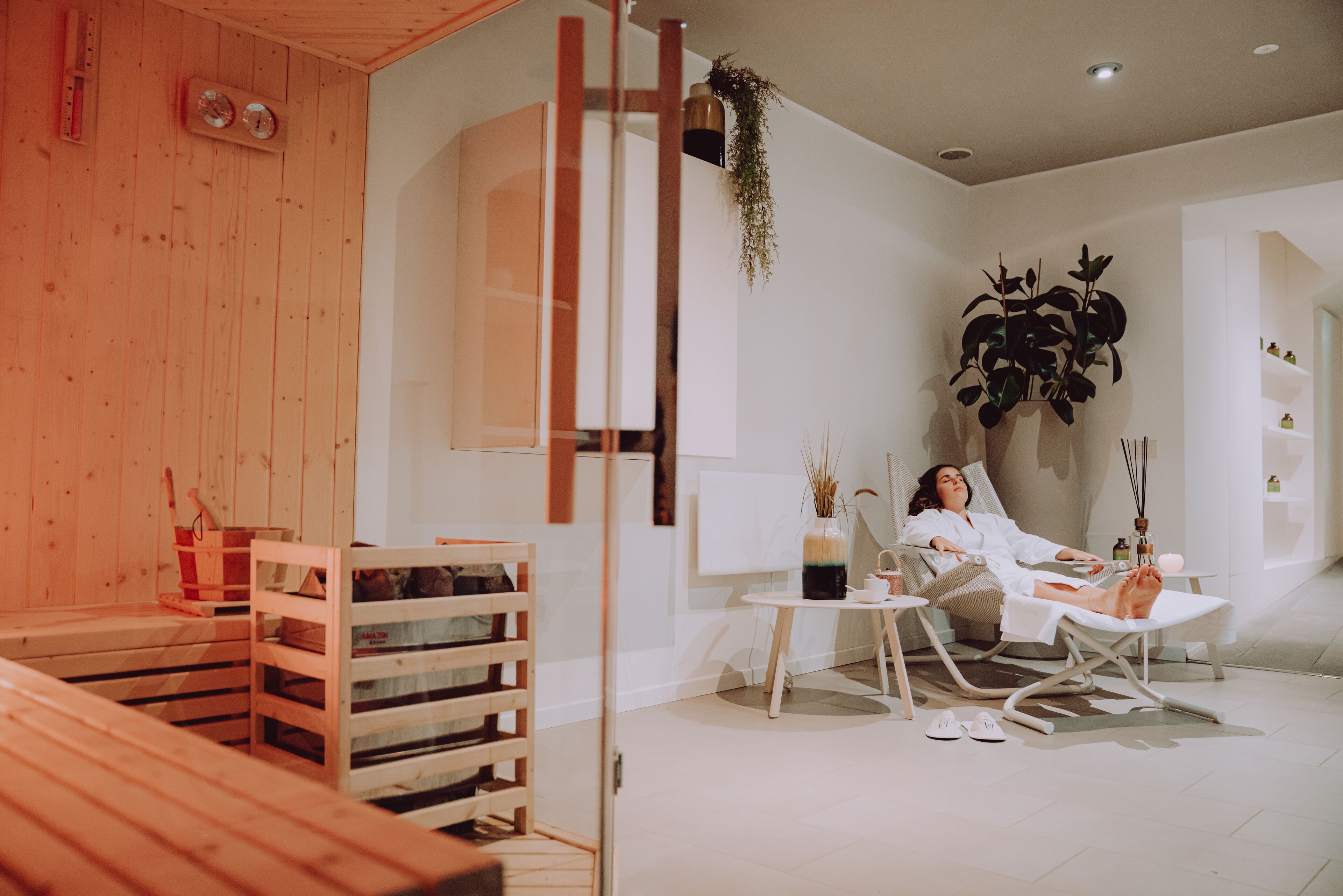 Un cuarto de spa con un banco de madera, una camilla de masaje y una mesita con un florero y velas.