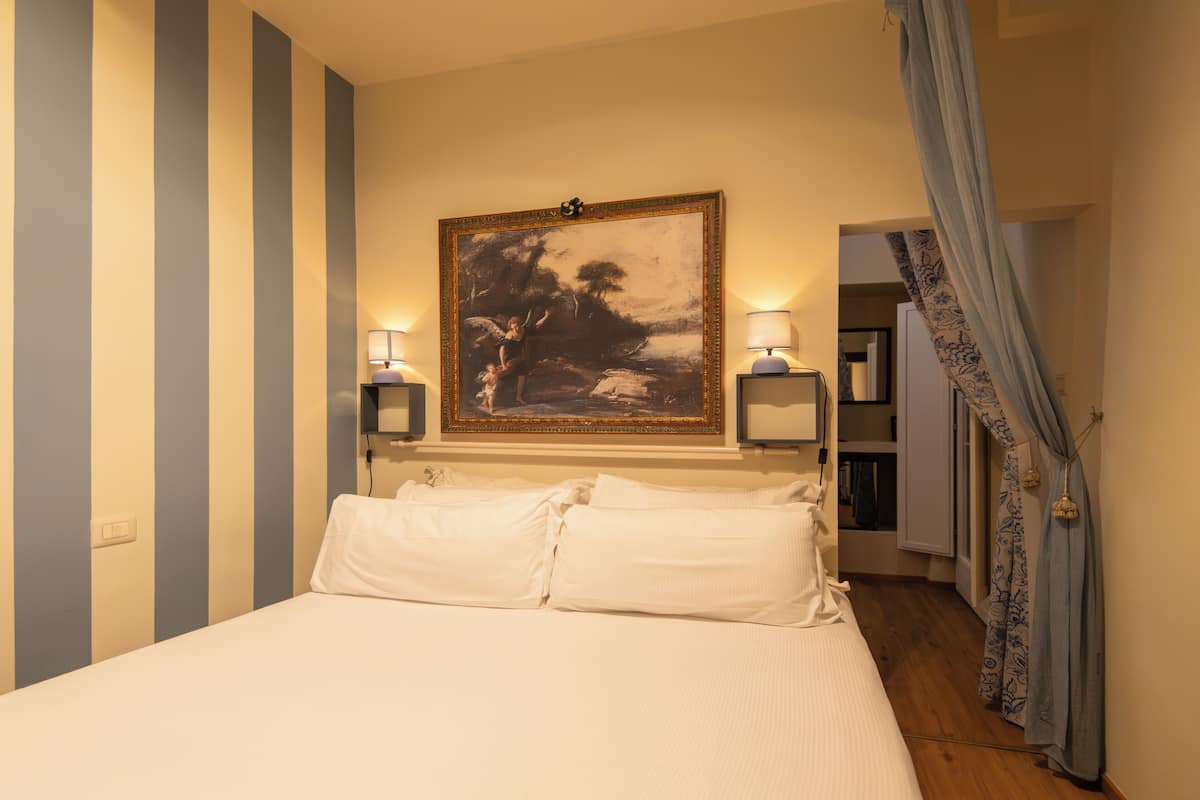 Ein Hotelzimmer mit einem großen Bett, zwei Nachttischlampen, einem gerahmten Gemälde über dem Bett und einer Tür zu einem anderen Raum.
