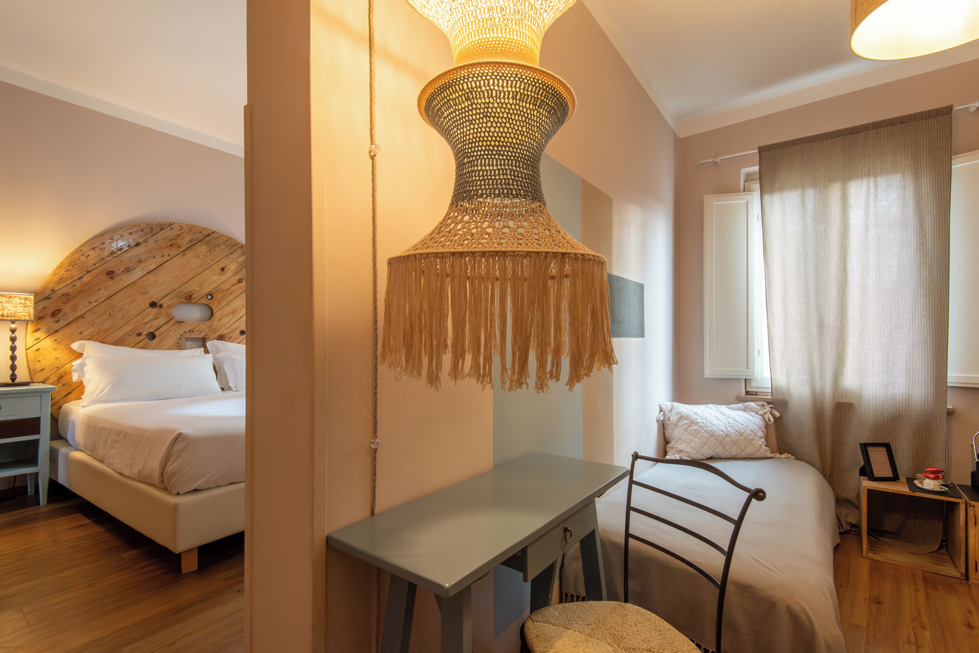 Un dormitorio con cama, escritorio, silla, lámpara colgante y ventana con cortinas.