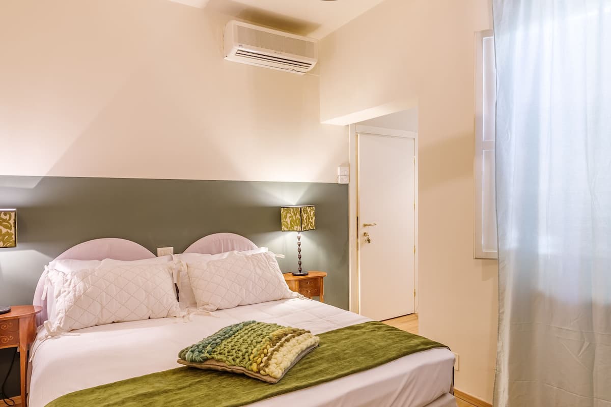 Ein Schlafzimmer mit einem Bett, einer Pendelleuchte, einer Tür und einem Fenster mit Vorhängen.