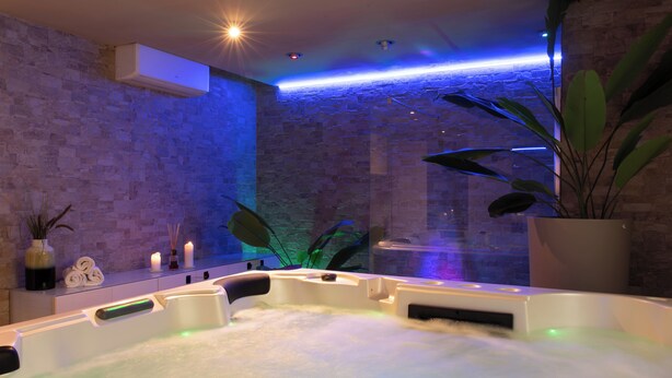 Een wellnessruimte met een jacuzzi, een bakstenen muur en een potplant.
