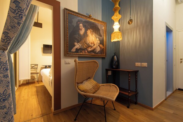 A room with a wicker chair, a painting on the wall, a television, and a wooden floor. - Boutique Hotel Aurora (Spoleto)