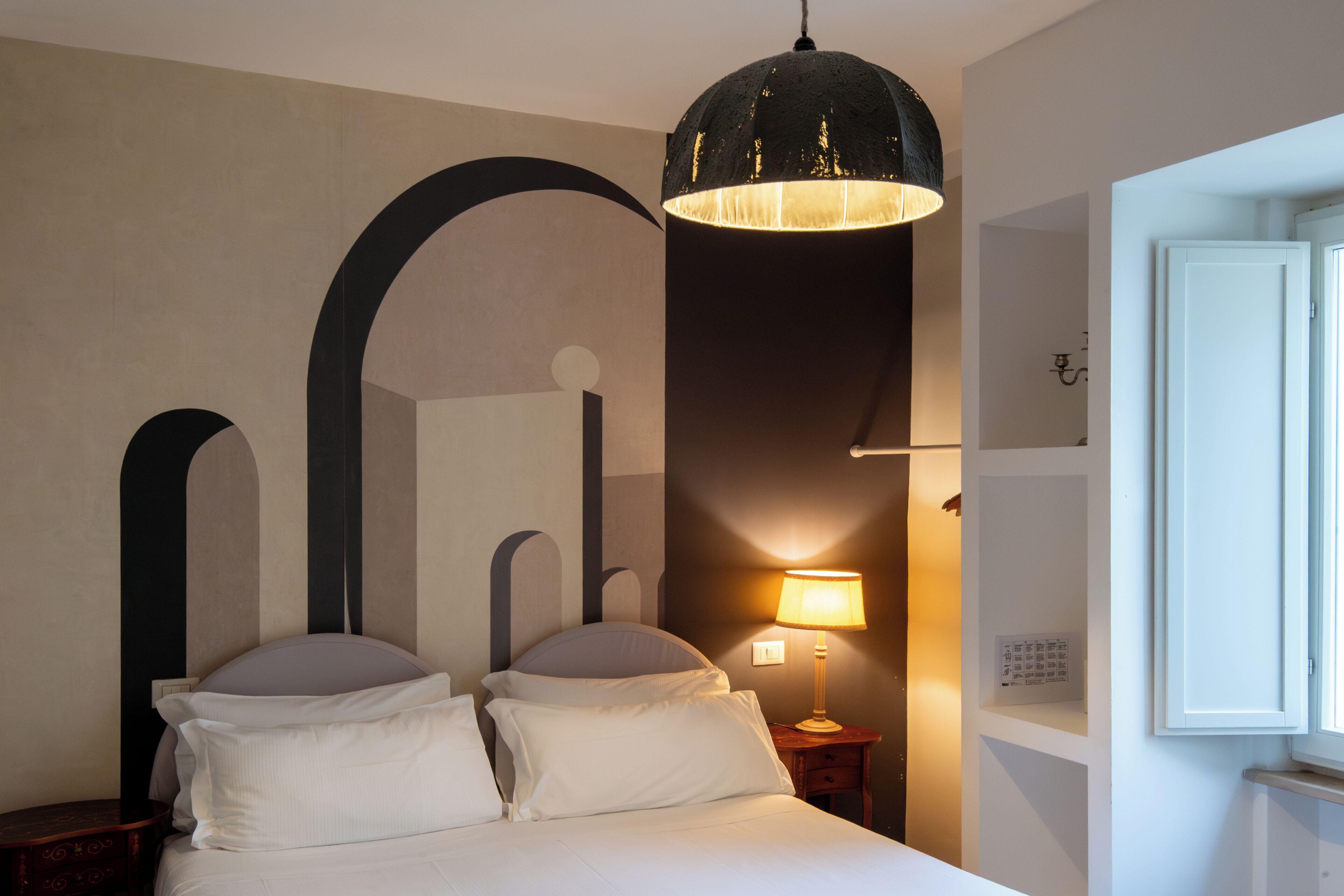 A hotel room with a bed, a nightstand, a lamp, and a large window.