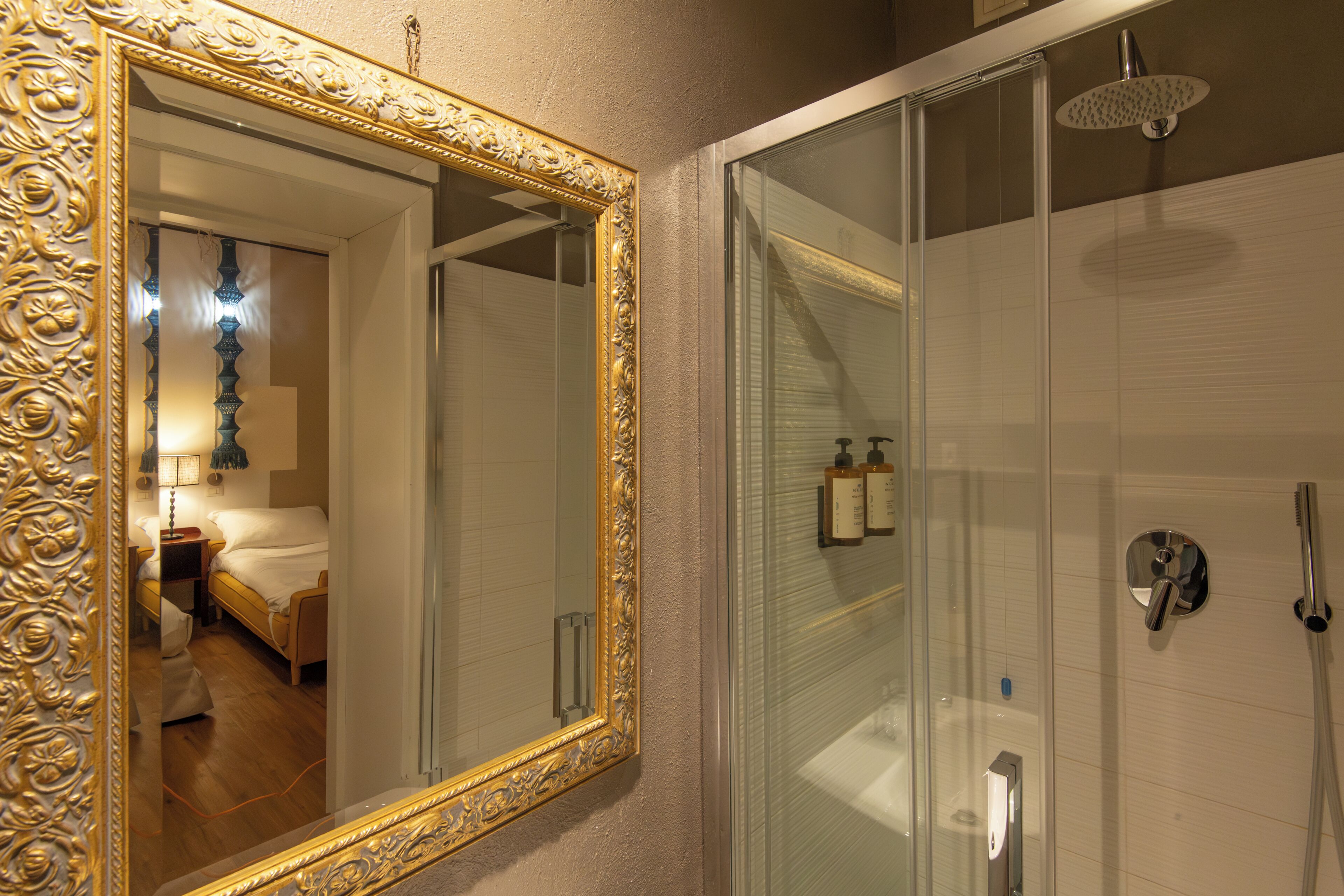 A bathroom with a glass shower enclosure, a gold-framed mirror, and a visible bathroom sink.