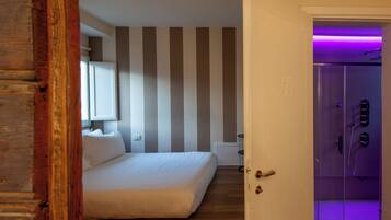 Une chambre avec un lit, un plancher en bois, un mur à rayures et un espace douche éclairé de lumières violettes.