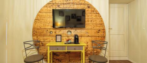 A room with a wooden wall, a TV mounted above a yellow desk, two chairs, and a door.