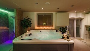 Een moderne wellnessruimte met een jacuzzi, kaarsen en een grote kamerplant.