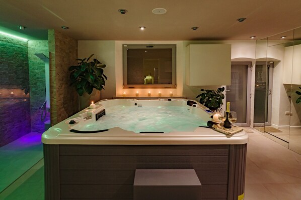 Un espacio de spa moderno con un jacuzzi, velas y una planta grande en maceta.