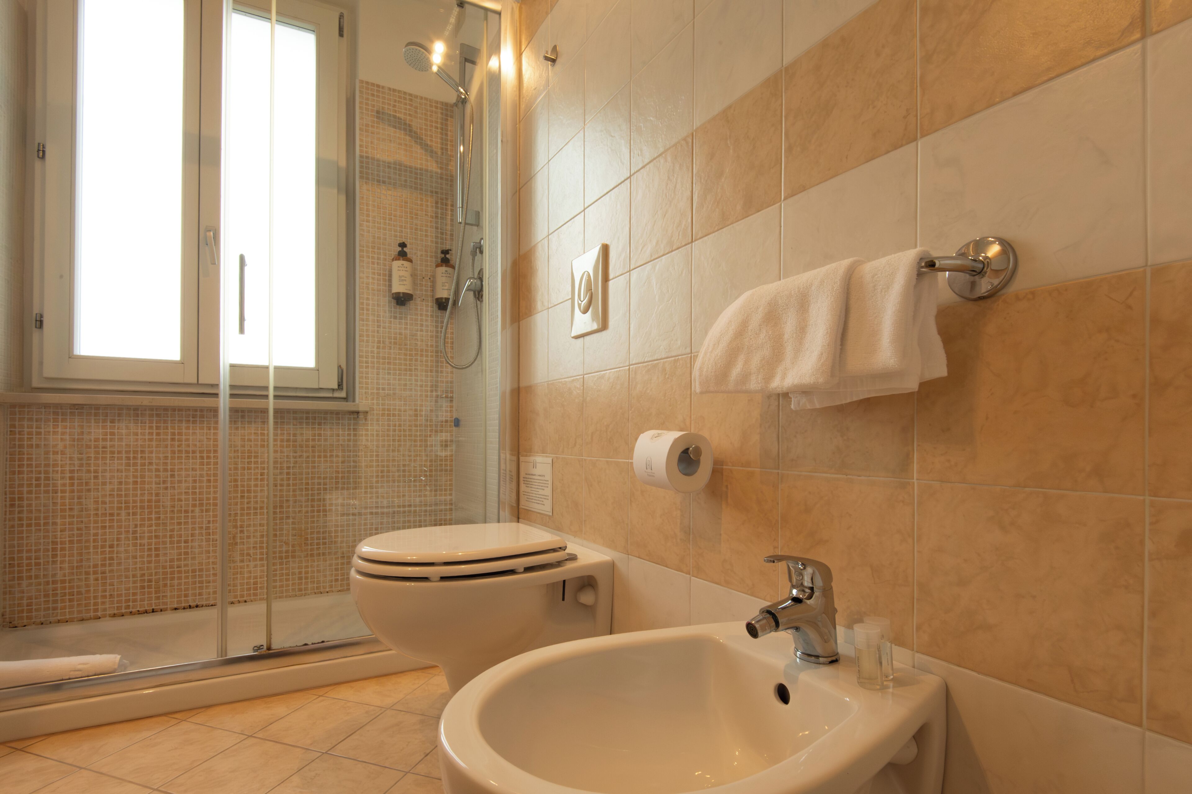 Une salle de bain comprenant des toilettes, un bidet et un lavabo, ainsi qu’une douche avec des portes en verre et une serviette suspendue à un porte-serviettes.