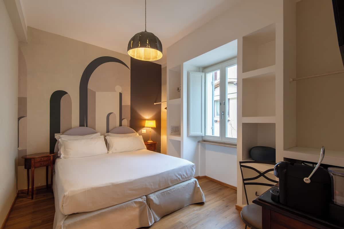 Ein Schlafzimmer mit Bett, Nachttisch, Lampe und Blick auf die Straße durch ein Fenster.