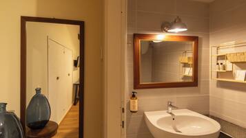A bathroom with a white sink, a mirror with a wooden frame, and a shelf with toiletries.