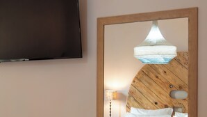 Een slaapkamer met een bed, een spiegel, een televisie en rieten stoelen.