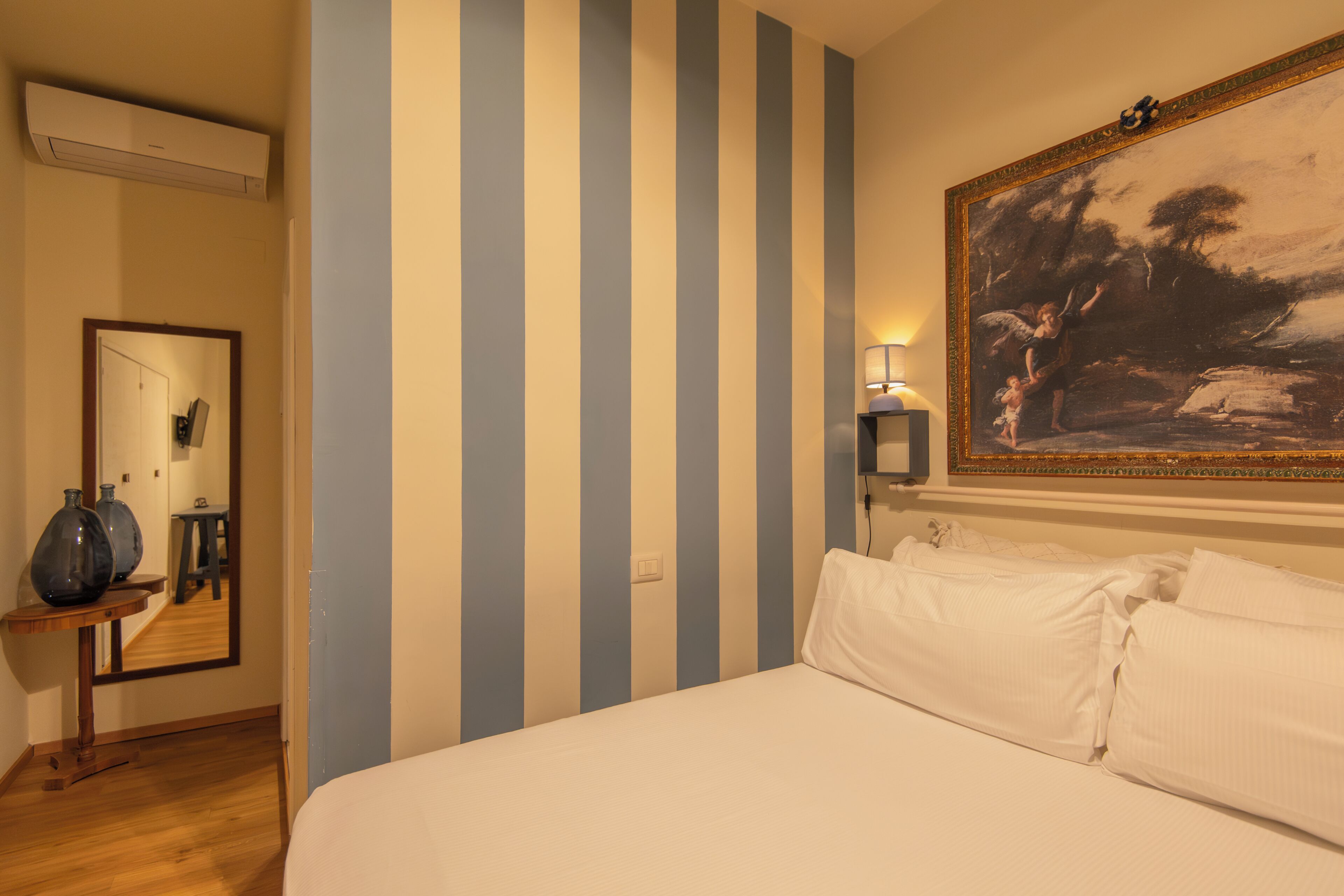 A hotel room with a bed, a large painting, a mirror, and a lamp.