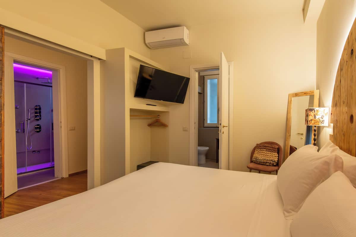 Ein Hotelzimmer mit Bett, einem an der Wand montierten Fernseher, einer Dusche und einer Holztür.