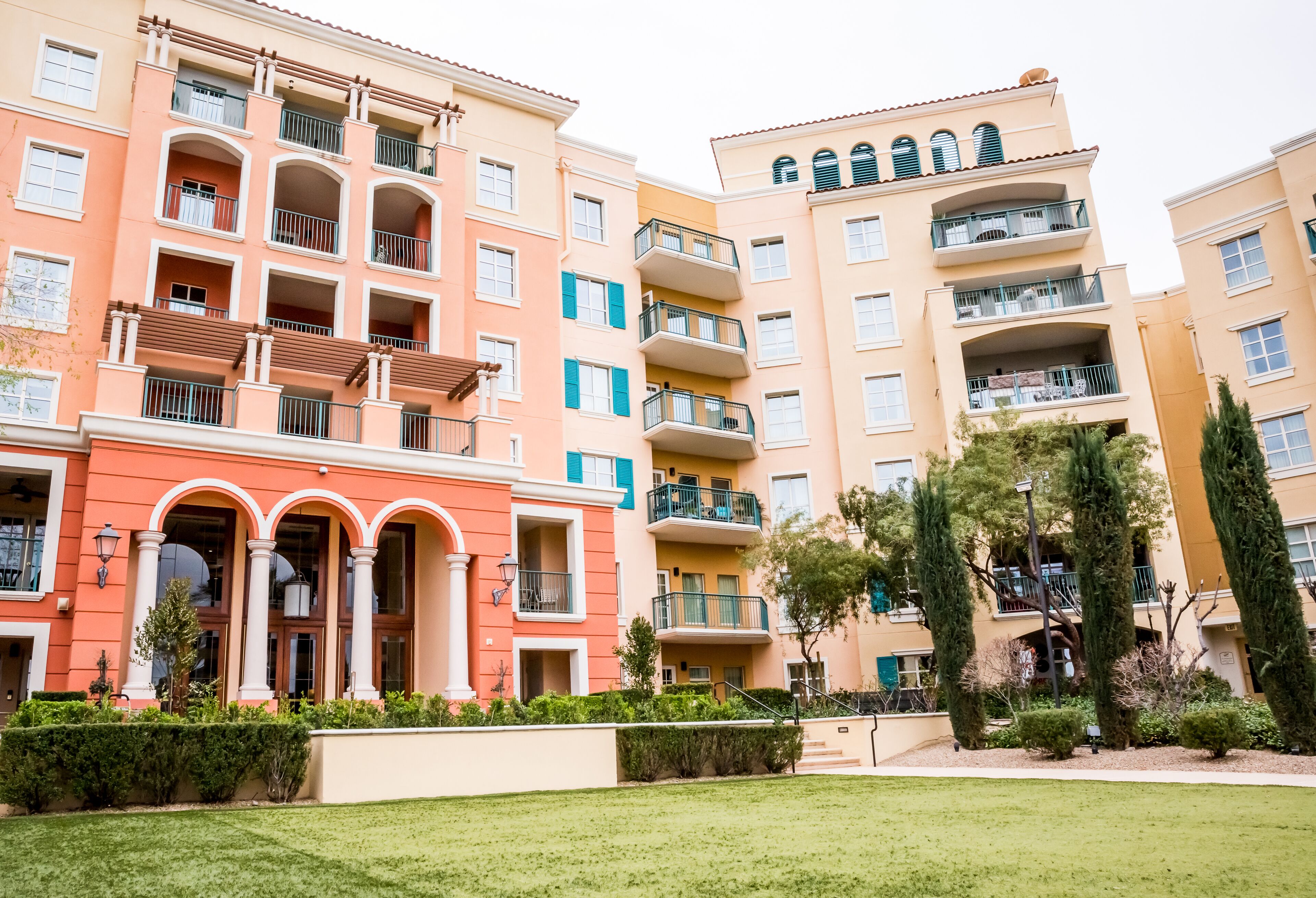A multi-story residential building with balconies, a central courtyard, and a well-maintained lawn.