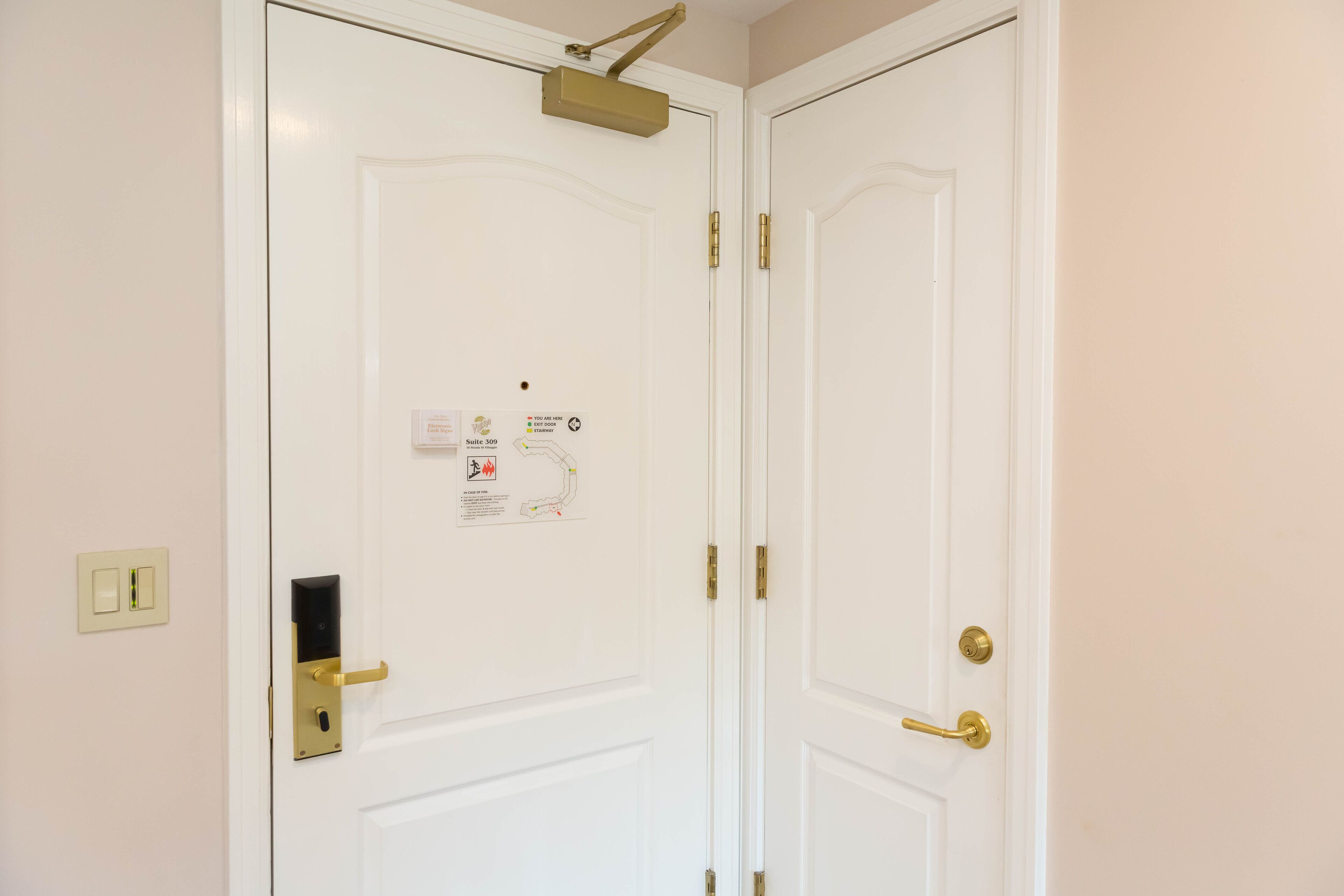 A white door with a brass handle, a lock, and a light switch on the wall.