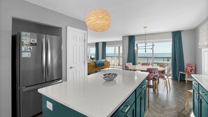 Una cocina moderna con una isla grande, electrodomésticos de acero inoxidable, armarios color turquesa y vistas al exterior.
