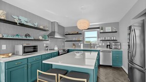 Una cocina moderna con armarios color turquesa, una isla grande, electrodomésticos de acero inoxidable y objetos decorativos en estantes.