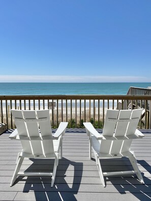 Una terraza de madera con sillones blancos que dan a la playa.