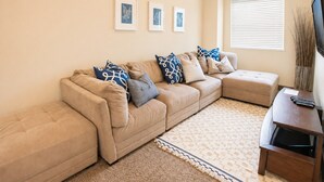 A living room with a beige sectional sofa, a patterned rug, and framed artwork on the wall. - Two heated pools/spas, pond, backyard w/ BBQ (Washington)