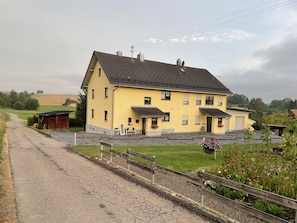 A yellow two-story house with a paved driveway and a wooden fence.
