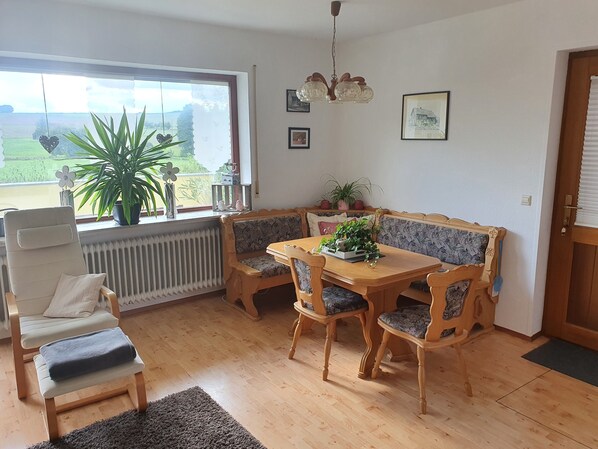 A cozy dining area with a wooden table and matching chairs, a bench, a radiator, and a window with a view of greenery.