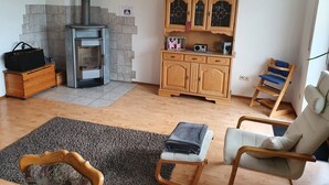 Een gezellige woonkamer met een open haard, houten kasten, een bank en een fauteuil.