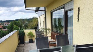 Een balkon met een tafel en stoelen, plantenpotten en uitzicht op de omgeving.
