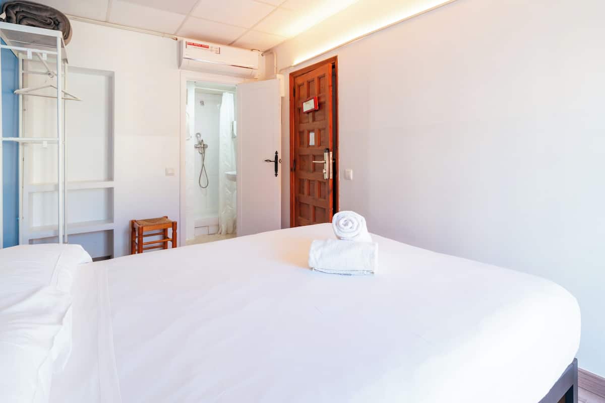 Habitación de hotel con una cama grande, una puerta de madera, zona de ducha y armario.