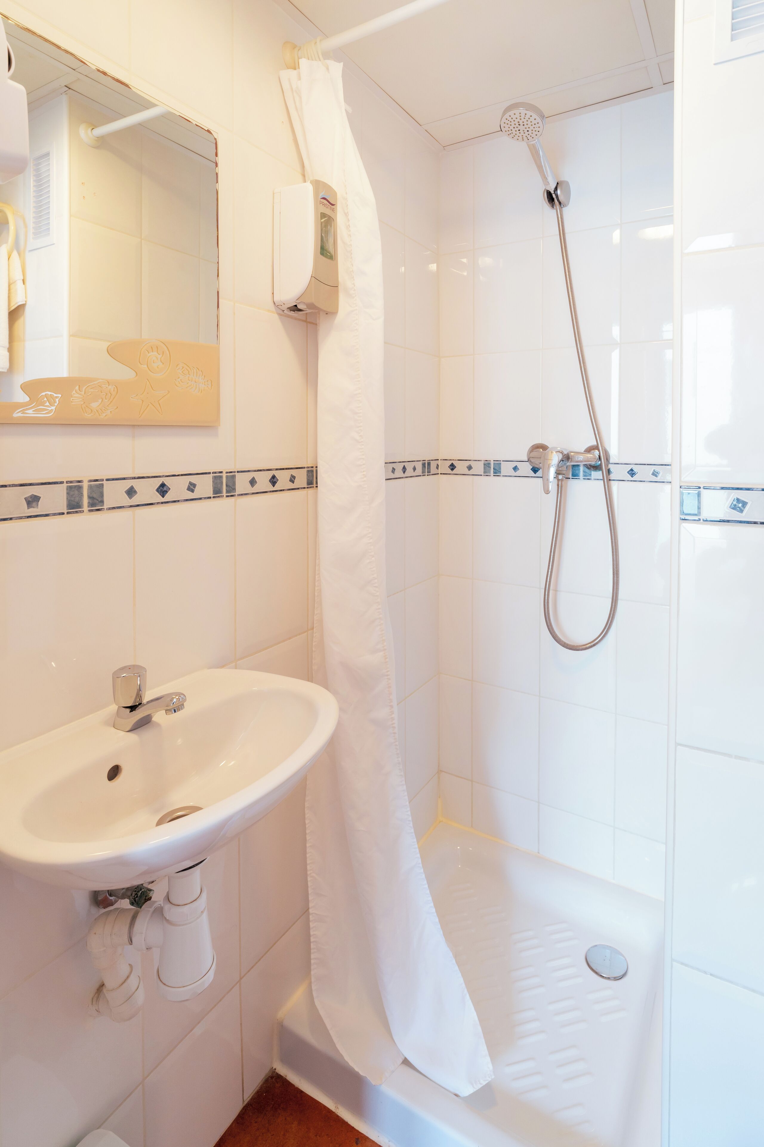 Un baño con un lavabo blanco, una ducha con cabezal de ducha manual y una toalla colgada en la pared.