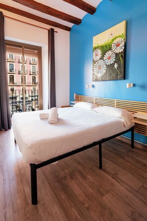 A neatly made bed with white linens and towels, a wooden headboard, and a painting of daisies on the wall. - Hostal Forum Tarragona (Tarragona)