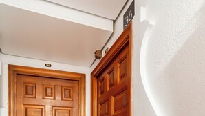 A wooden door with a number plate, adjacent to a wall with a white textured surface and a number plate. - Hostal Forum Tarragona (Tarragona)