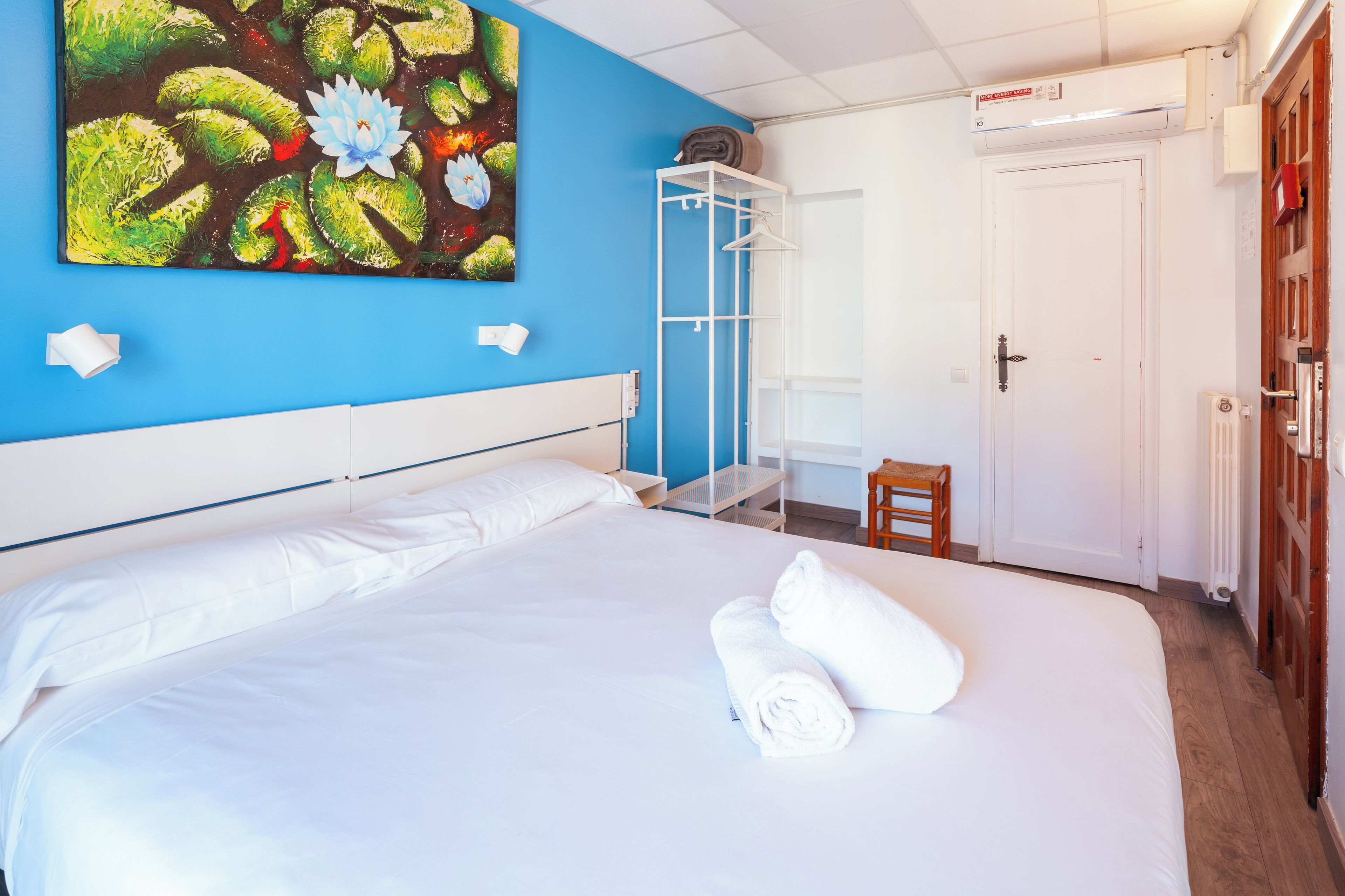Quarto de hotel com uma cama grande, uma parede de destaque azul, um guarda-roupa branco e um quadro com flores.