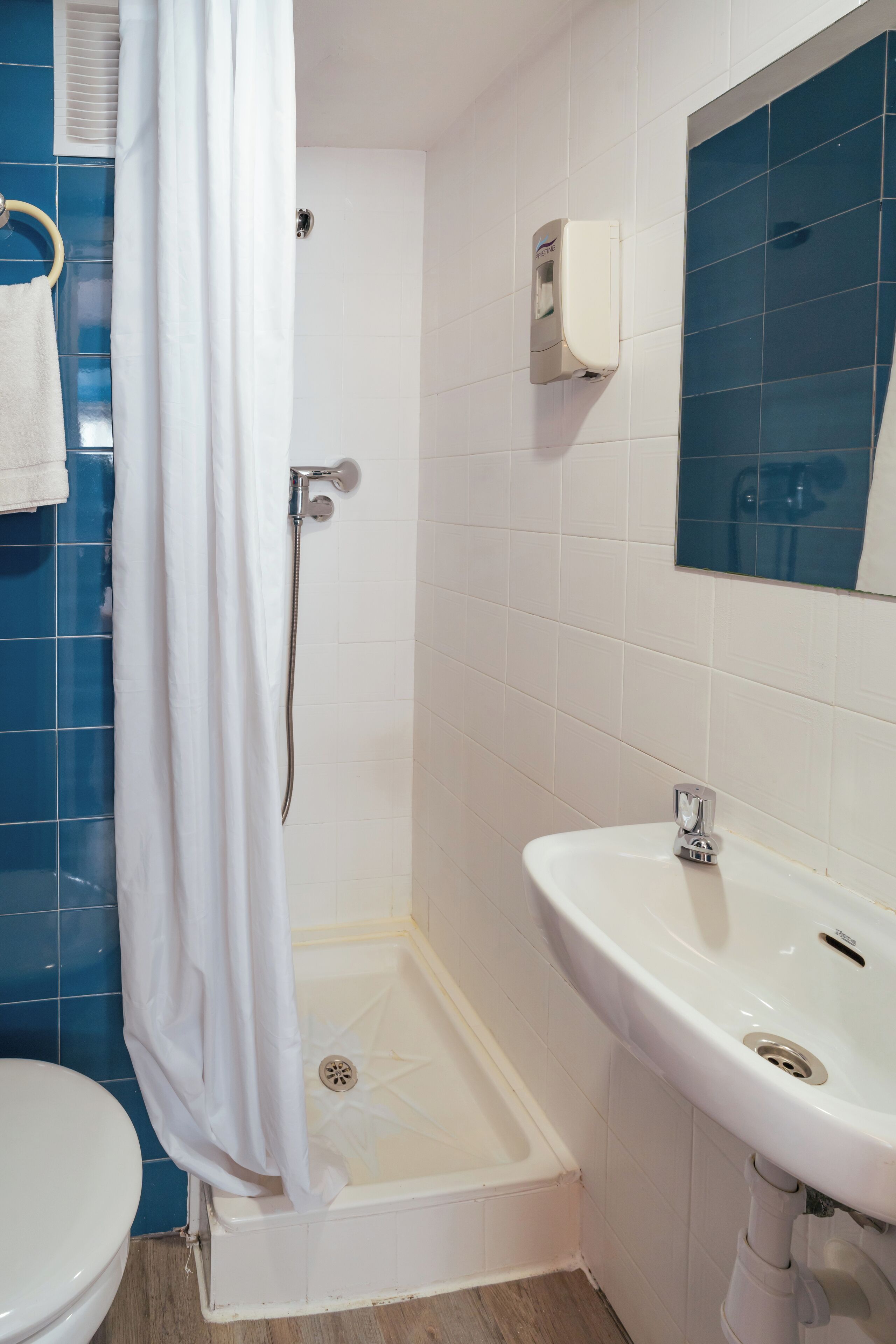 Un baño con lavamanos blanco, ducha con cortina blanca y paredes de azulejos azules.