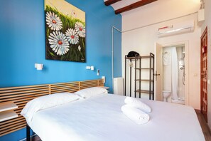 A bedroom with a large bed, a painting of daisies, a wooden headboard, a radiator, and a shower area. - Hostal Forum Tarragona (Tarragona)