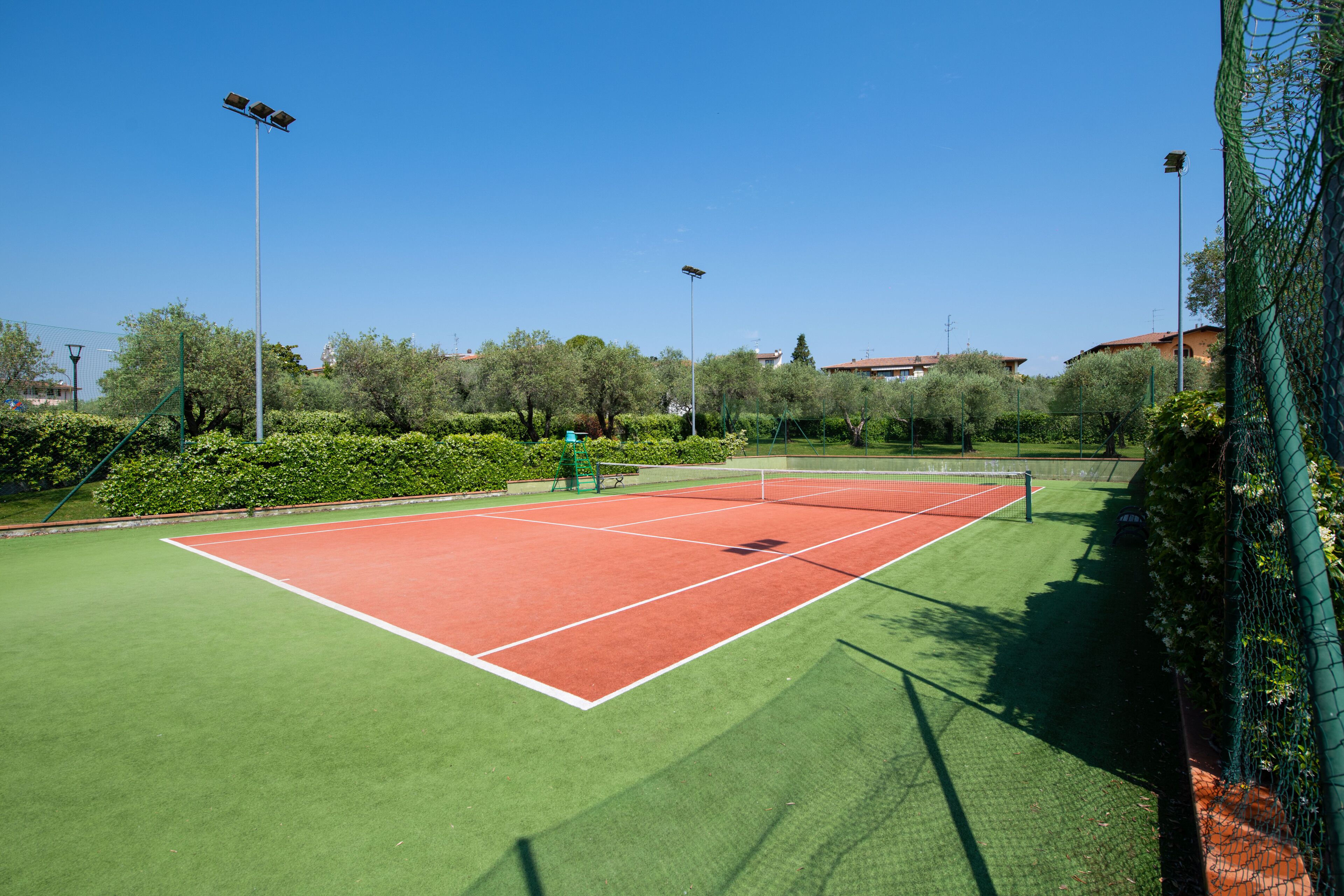 Een tennisbaan met groene en rode oppervlakken, omringd door bomen en een hek.