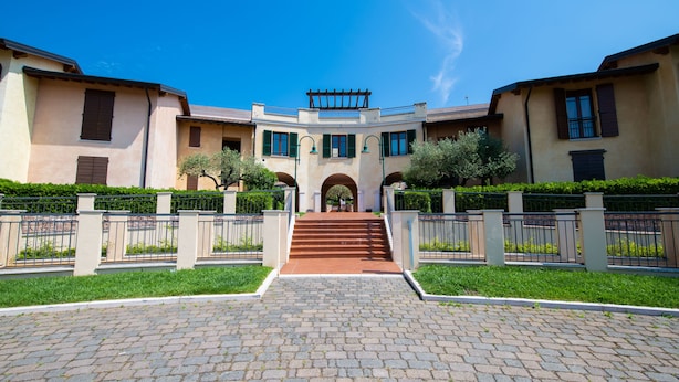 A building with a central staircase leading to an entrance, flanked by two wings with windows and greenery. - Appartamento Victoria (Manerba del Garda)