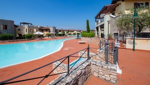 A pool area with lounge chairs and a stone wall. - Appartamento Victoria (Manerba del Garda)