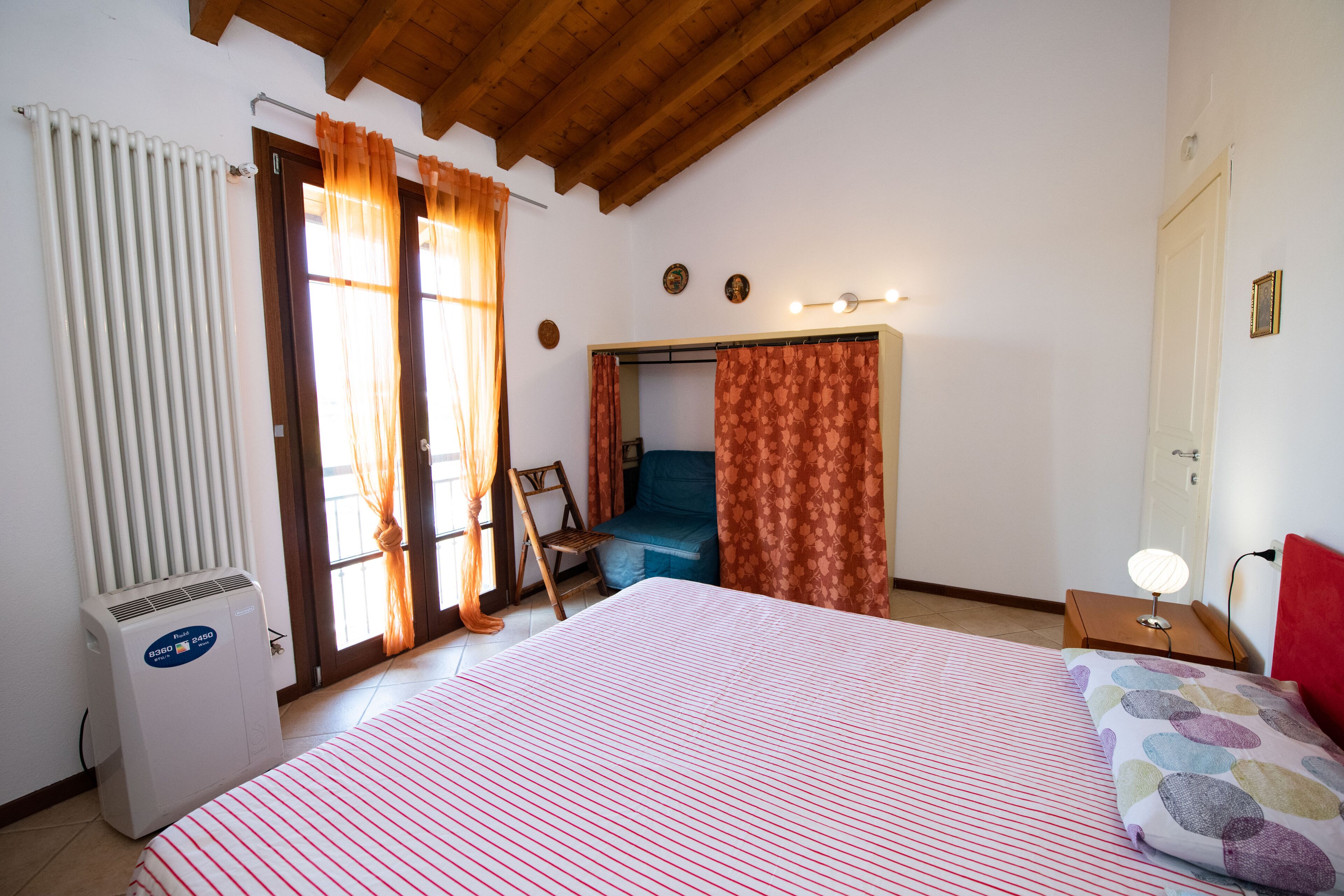 Une chambre à coucher avec un lit, un radiateur, une chaise, un bureau avec une lampe et une porte.