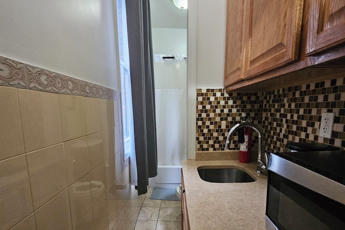 Una cocina con salpicadero de azulejos, un lavamanos de acero inoxidable, armarios de madera y un microondas.