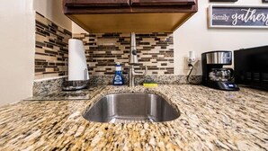 A kitchen with granite countertops, a stainless steel sink, wooden cabinets, a coffee maker, and a wall-mounted sign that says "family gatherings". - Shefah Hotel (Union City)