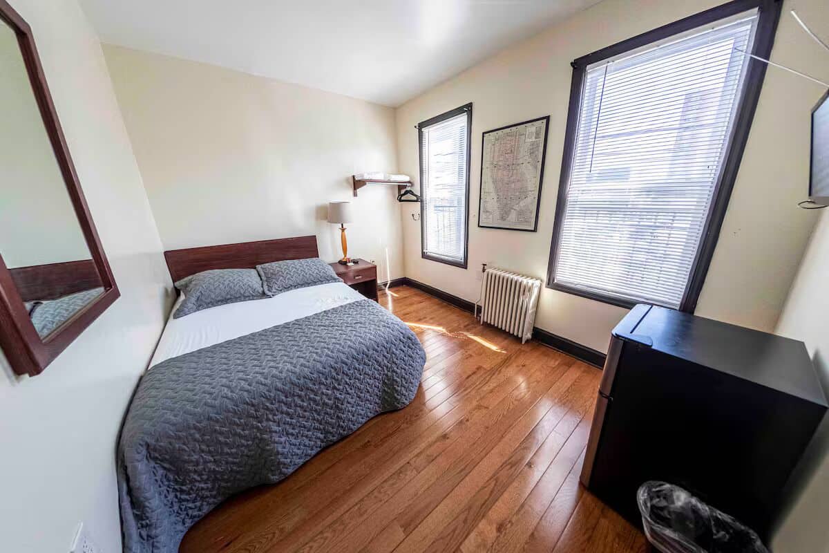 Un dormitorio con cama, mesita de noche, lámpara, radiador y ventana con persianas.