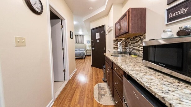 A narrow kitchen with wooden flooring, a granite countertop, a microwave, and wooden cabinets. - Shefah Hotel (Union City)