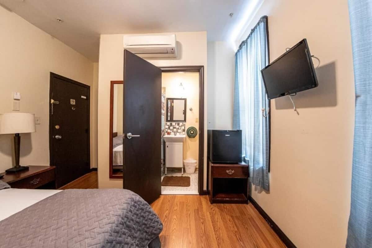 Una habitación de hotel con cama, televisor montado en la pared, puerta que da al baño y aire acondicionado.