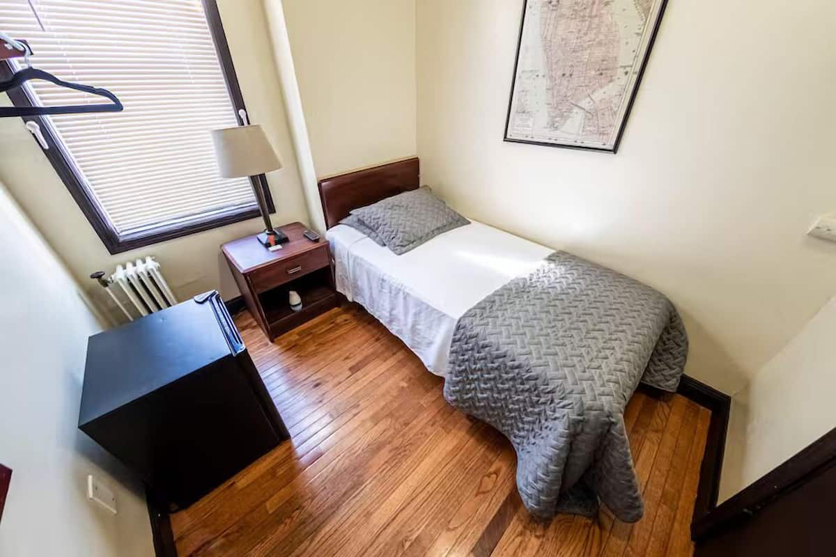 Un dormitorio pequeño con cama, mesita de noche, lámpara, radiador y un mapa en la pared.