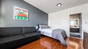 A modern room with a gray sofa, a bed with a gray blanket, and a wooden floor. - Shefah Hotel (Union City)