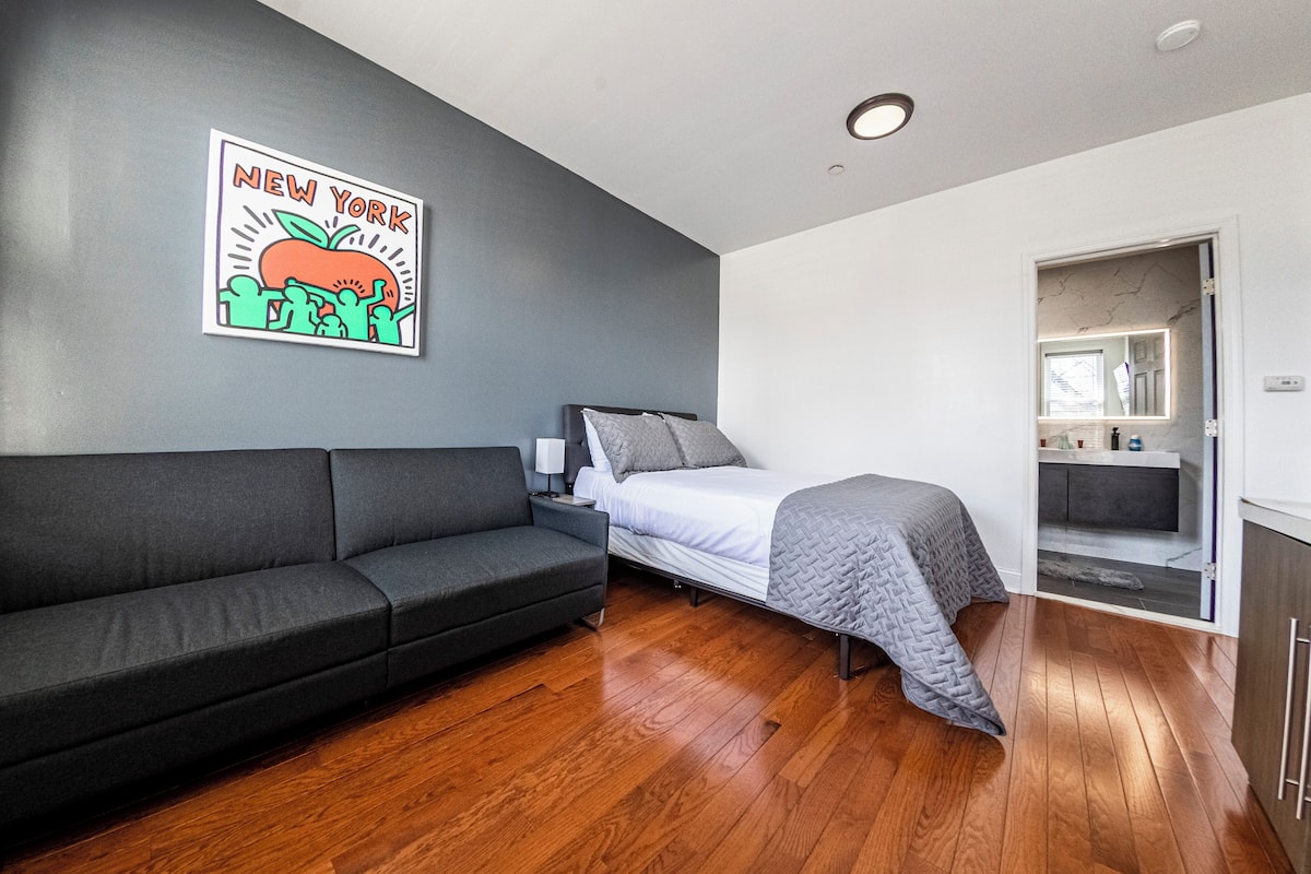 Una habitación moderna con un sofá gris, una cama con manta gris y suelo de madera.