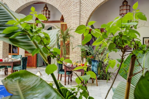 A courtyard with a dining table and chairs, surrounded by plants and a tiled floor. - Riad Janate & SPA - Suite Supérieure (Marrakesh)