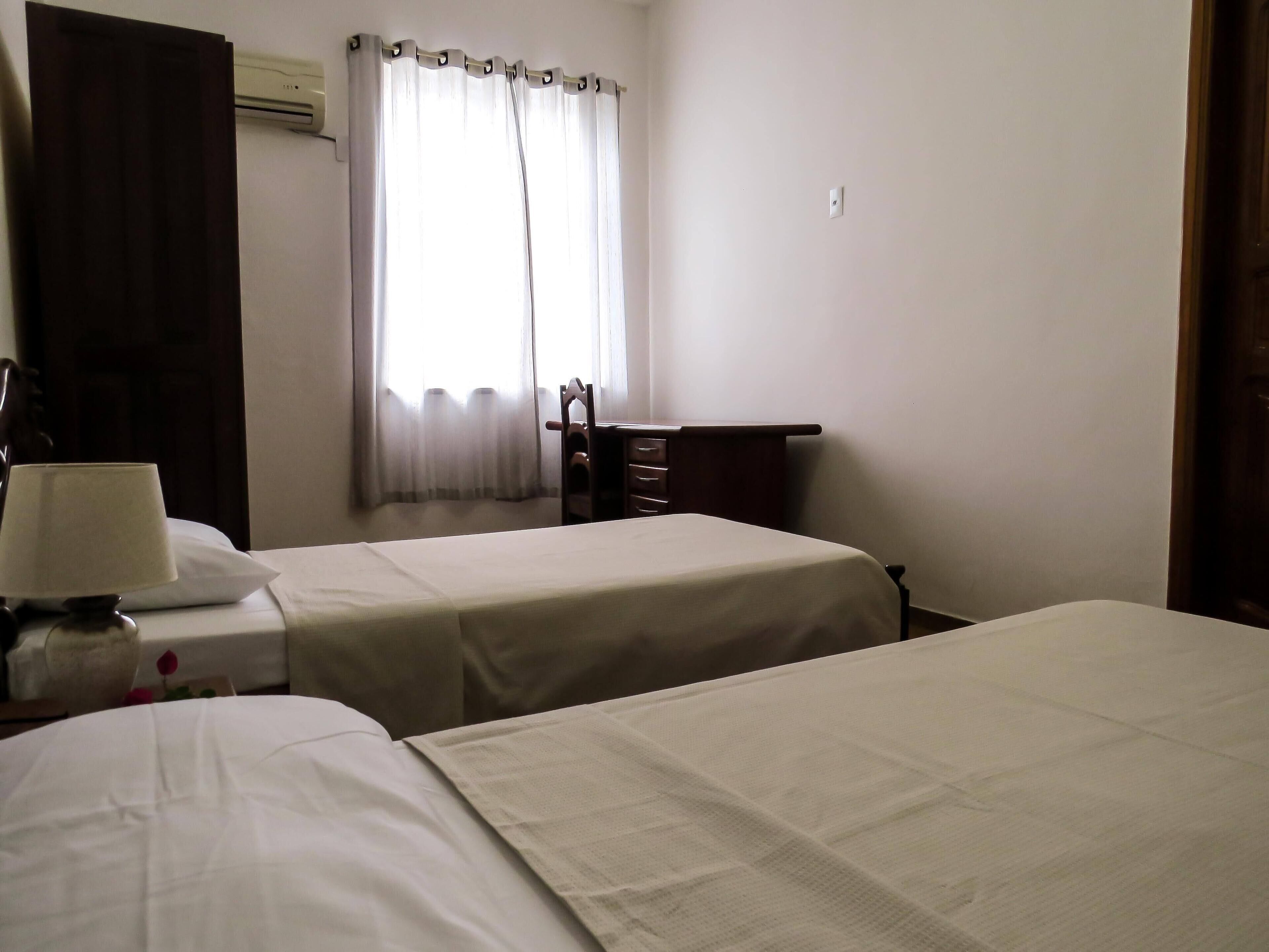 A hotel room with two beds, a desk, a chair, and a lamp.