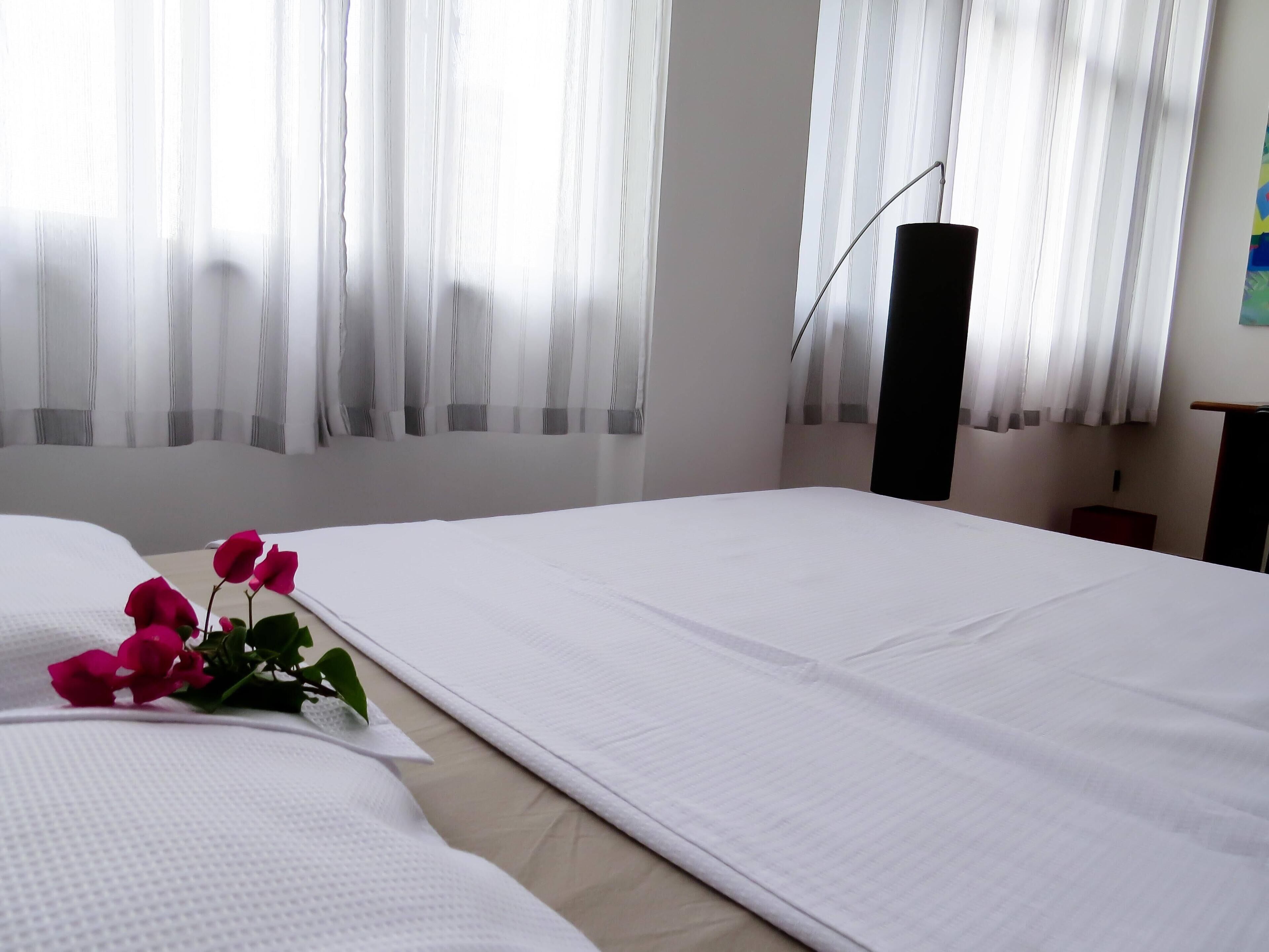 A hotel room with a neatly made bed, a bedside table, and a lamp.